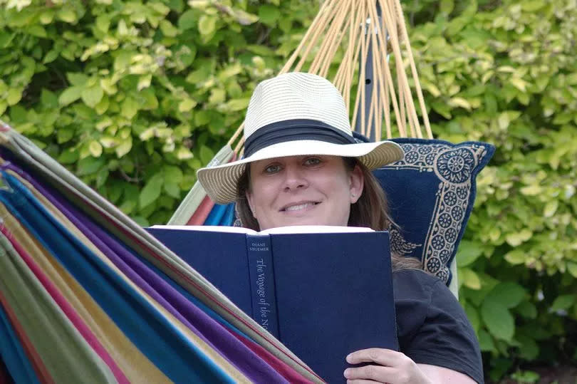 Woman sitting in a hammock, reading her book with a hat on
