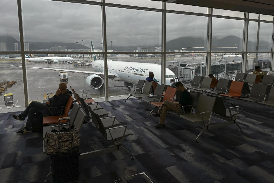 Travelers wait at the departures hall as aircraft operated by Cathay Pacific Airways taxing at Hong Kong International Airport in Hong Kong, Sunday, Oct. 8, 2023. Scores of flights in Hong Kong were canceled Sunday as Tropical Storm Koinu neared the southern Chinese city after leaving at least one dead and over 300 injured in Taiwan. (AP Photo/Emily Wang)