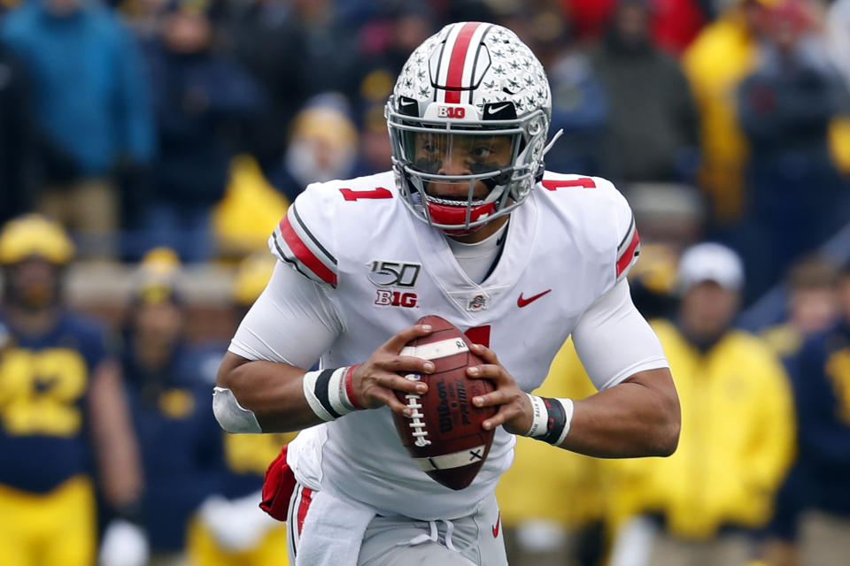 FILE - In this Nov. 30, 2019, file photo, Ohio State quarterback Justin Fields rolls out to throw against Michigan during the first half of an NCAA college football game in Ann Arbor, Mich. Ohio State opens preseason training camp on Thursday, Aug. 6, 2020, with strict coronavirus protocols in place and under a cloud of uncertainty about whether a revised 10-game season will even be played at all. (AP Photo/Paul Sancya, File)