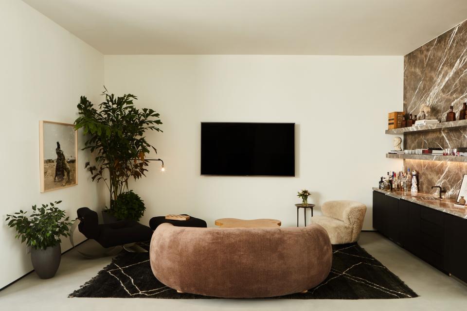 A chocolate-brown mohair sofa from JF Chen and the Cloud coffee table by Paul Frankl take center stage and sit on a vintage carpet from Marrakech. On the right, the custom bar in honed bronze vena stone is from Stoneland and the Danish 1940s Viggo Boesen–style lounge chair upholstered in cream shearling is next to a Rick Owens bronze side table. On the left, the Alta single armchair by Oscar Niemeyer combines with the Jean Prouvé Swing Jib lamp.