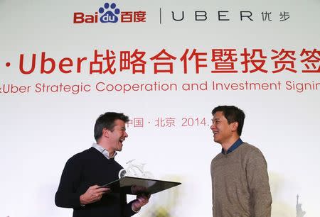 Uber CEO Travis Kalanick (L) smiles after receiving a gift from Baidu Inc. Chairman and CEO Robin Li after signing their documents during the Baidu and Uber strategic cooperation and investment signing ceremony at Baidu's headquarters in Beijing December 17, 2014. REUTERS/Kim Kyung-Hoon