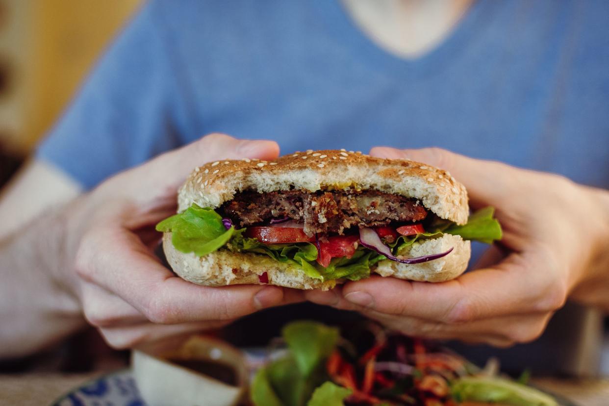 Closeup of man's hands holding vegan chickpea and bean burger with fresh greens, selective focus