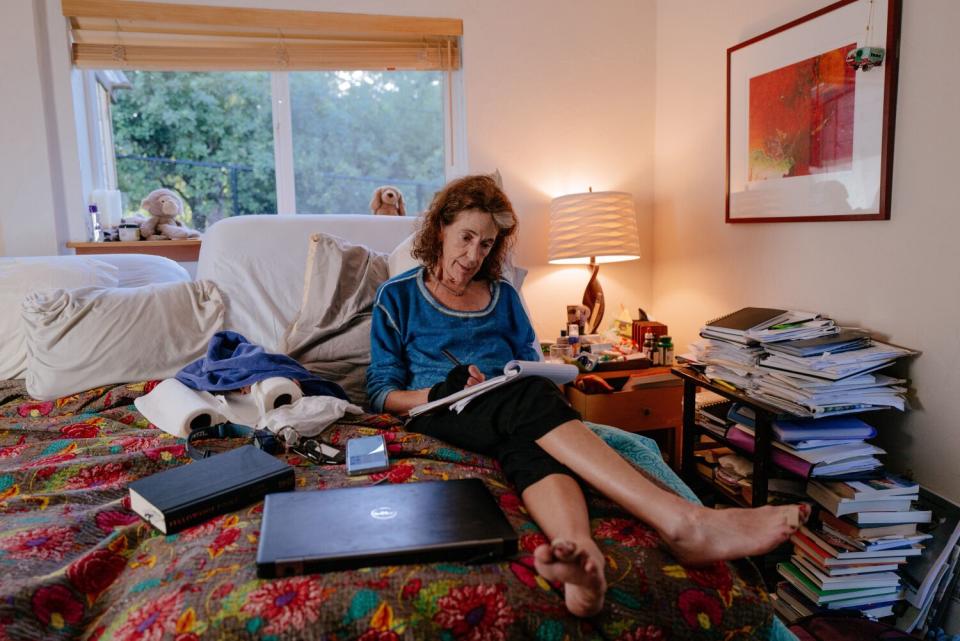 A woman sits cross-legged on a bed, writing on a pad of paper.