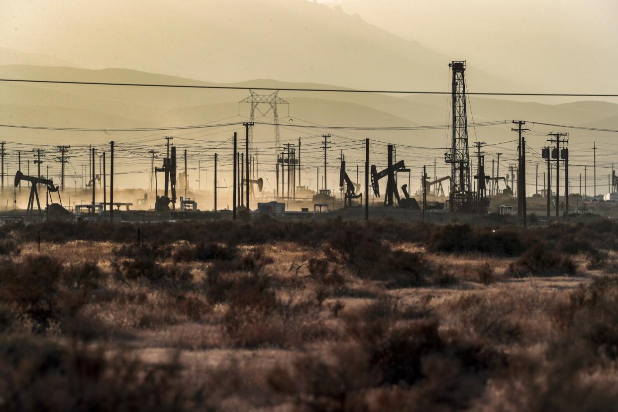 Oil pumpjacks and powerlines are silhouetted in a hazy oilfield.