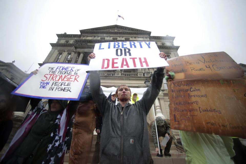 Protesters hold signs during a rally at the State Capitol in Lansing on Thursday, May 14, 2020.