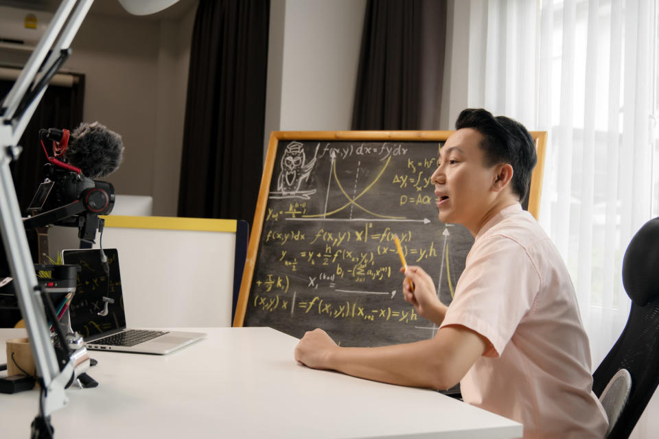 A teacher teaching a virtual class with a chalkboard