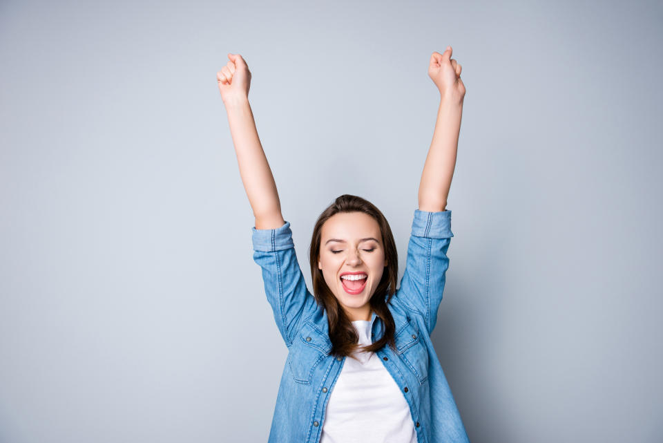 Amazed brunette young business woman in casual shirt is gesturing victory with her raised hands.