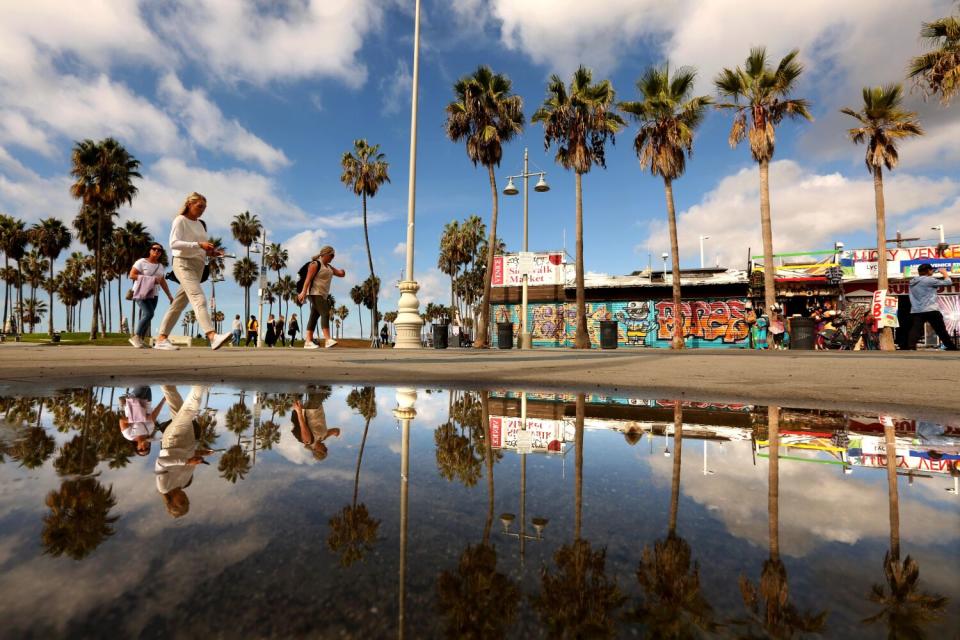 A rain puddle reflects clouds as pedestrians walk along Windward Avenue in Venice.