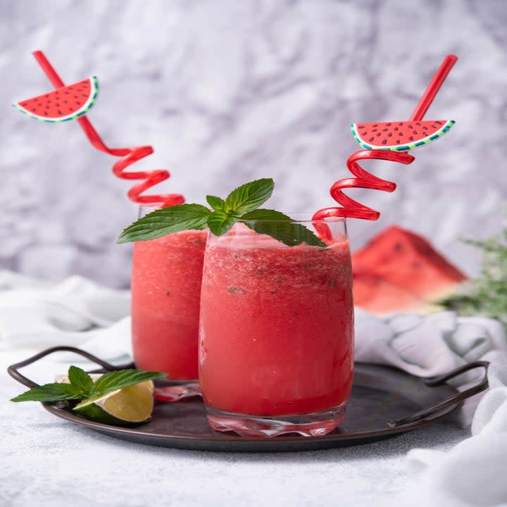 two pink smoothies made from watermelon in glasses with curly straws