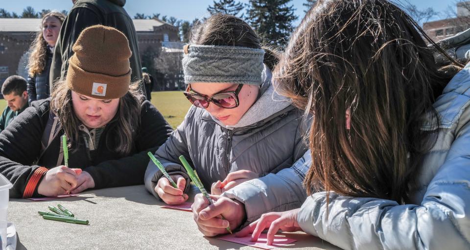 Michigan State students from left, Sofie Piotrowski, from Chicago, Cheyanne Schlinke, from Detroit, and Ellie Barron from Troy, write down their thoughts about the mass shooting that happened in February on campus that killed three students and wounded five others at a Walk Together event at Demonstration Hall Field Sunday, March 19, 2023.