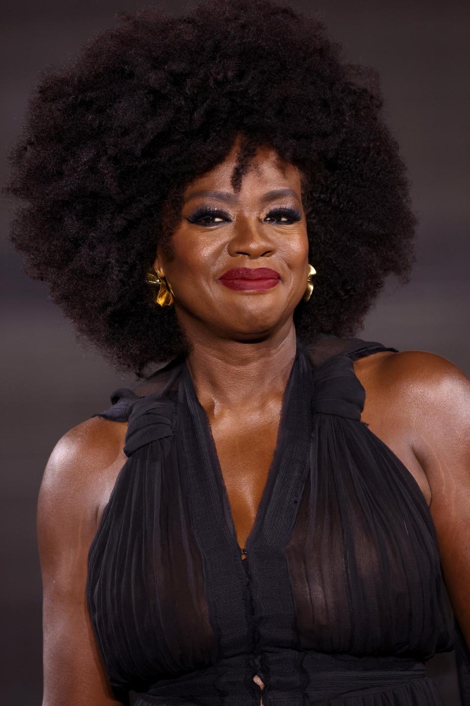 Viola with voluminous afro hair and a black sleeveless dress smiles