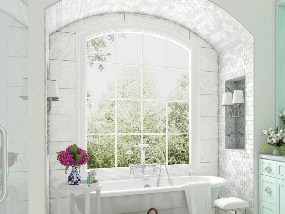 A white bathroom with mint cabinetry and a curved ceiling above the tub overlooking a window