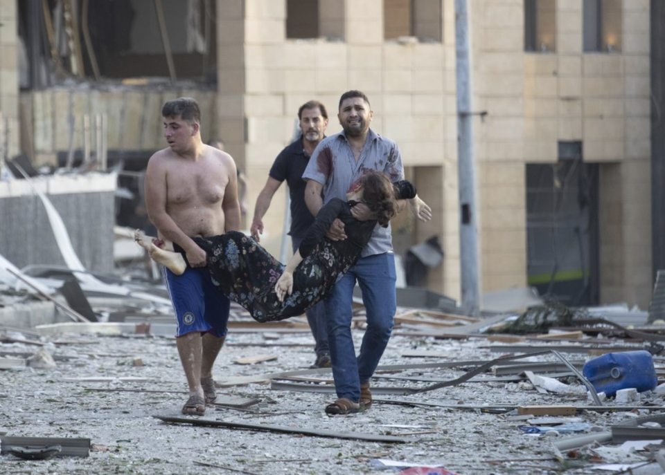 Two men carry a wounded woman through a Beirut street covered in debris.