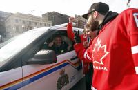 Fans celebrate Canada's gold medal win over Sweden in their men's ice hockey game at the Sochi 2014 Winter Olympic Games, with a member of the Royal Canadian Mounted Police (RCMP), on Parliament Hill in Ottawa February 23, 2014. The acronym GRC on the side of the police vehicle stands for Gendarmerie Royale du Canada, the French translation for RCMP. REUTERS/Chris Wattie (CANADA - Tags: POLITICS SPORT ICE HOCKEY OLYMPICS)