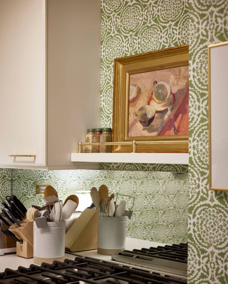 Art and spices above stove in wallpapered kitchen.