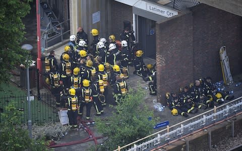Firefighters gather near the burning Grenfell Tower - Credit: Getty/Leon Neal