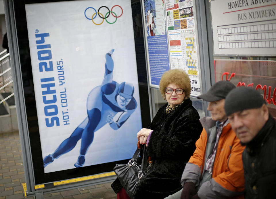 A woman waits for a bus next to a billboard advertising the upcoming 2014 Winter Olympics, Wednesday, Jan. 29, 2014, in Sochi, Russia. (AP Photo/David Goldman)