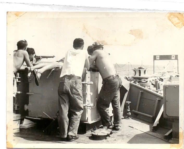 Crew members crowd around a gun on the deck of HMCS Haida during its Pacific deployment.