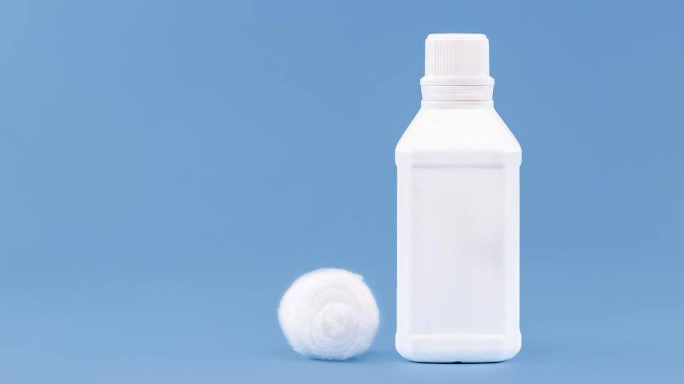 A white bottle of hydrogen peroxide next to a white cotton ball on a blue background