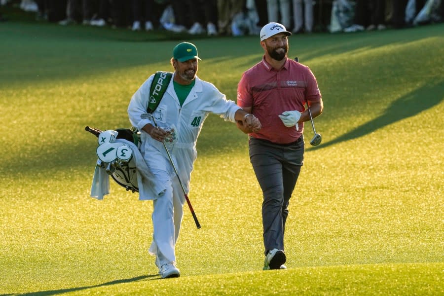 Jon Rahm, of Spain, grabs the hand of his caddie Adam Hayes as they approach the 18th hole during the Masters golf tournament at Augusta National Golf Club, in Augusta Georgia, Sunday, April 9, 2023. (AP Photo/Mark Baker)