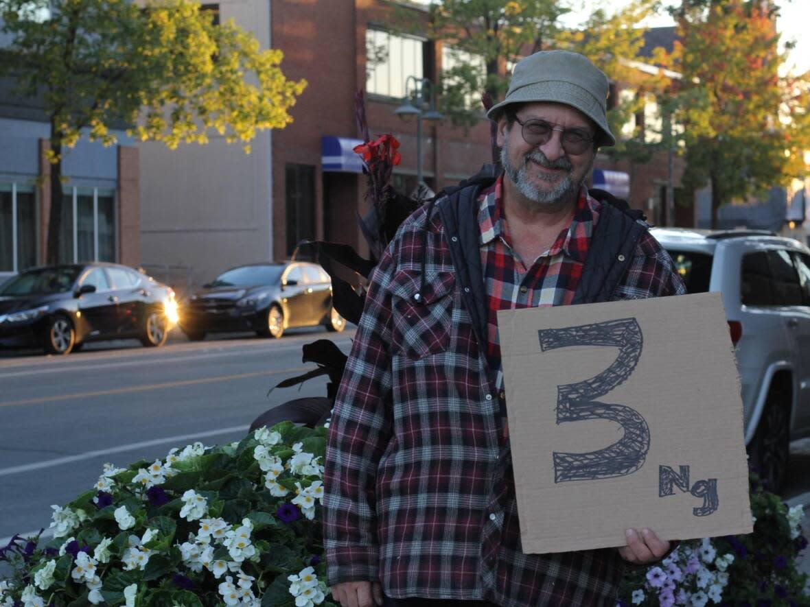 Rouyn-Noranda resident Denis Lafond holds a homemade sign outside the venue for a public meeting. Like many of his neighbours, he wants stricter rules to limit arsenic levels in the air to three nanograms per cubic metre. (Sandra Hercegova/CBC - image credit)