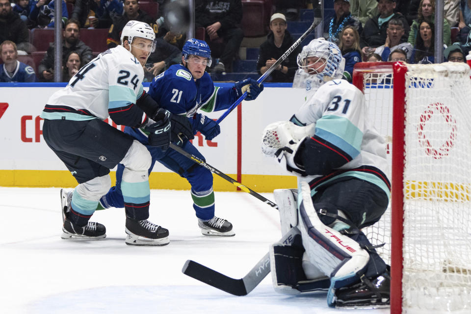 Seattle Kraken's Jamie Oleksiak (24) and Vancouver Canucks' Nils Hoglander (21) watch the puck after Kraken goaltender Philipp Grubauer (31) deflected a shot during the third period of an NHL hockey game Saturday, Nov. 18, 2023, in Vancouver, British Columbia. (Ethan Cairns/The Canadian Press via AP)