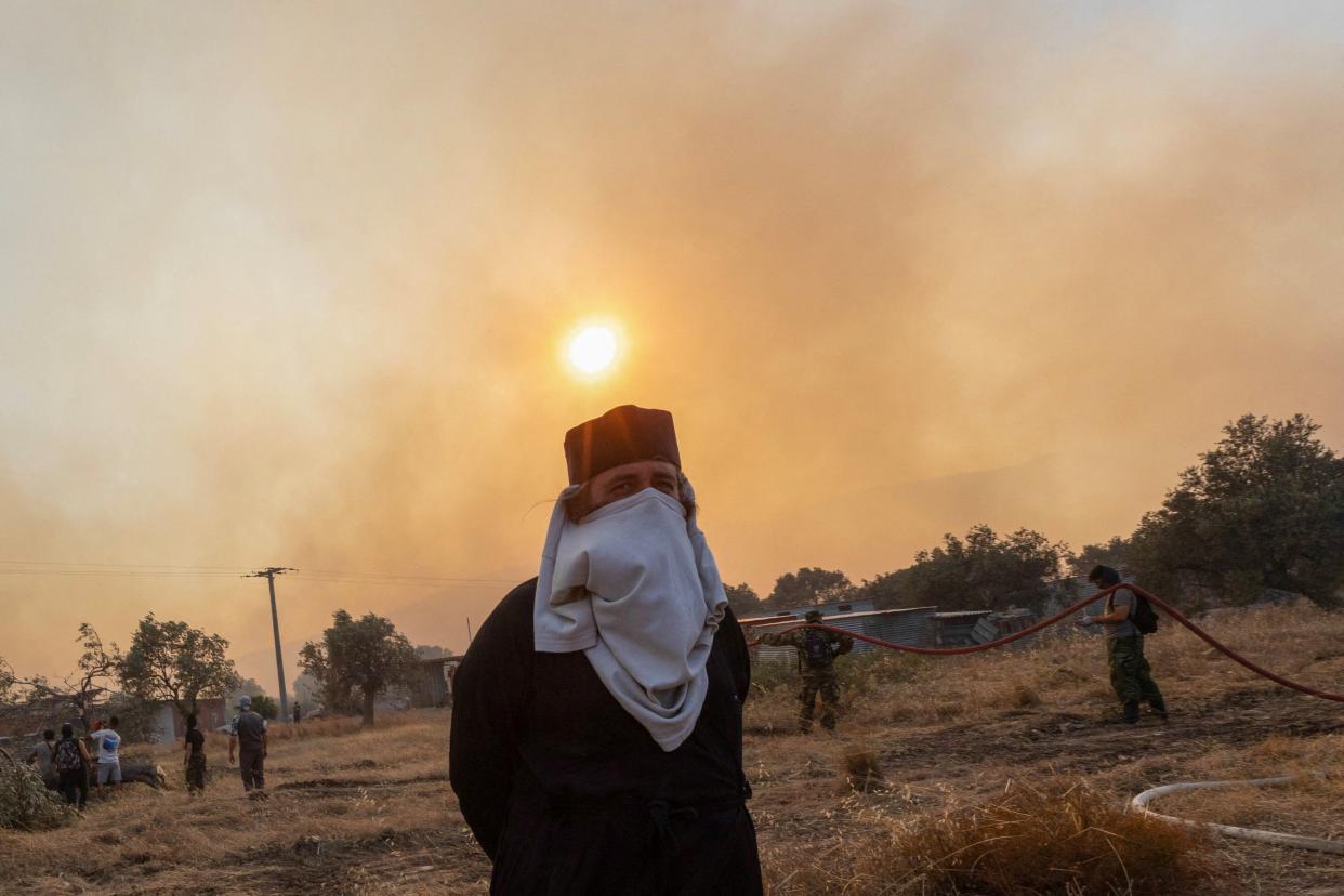 A Greek Orthodox priest covers his face to protect from smoke as firefighters, volunteers and police officers prepare to tackle a wildfire approaching the village of Masari, on the island of Rhodes (REUTERS)
