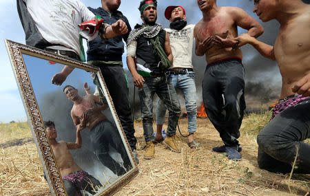 Palestinian protesters are seen reflected in a mirror during clashes with Israeli troops at the Israel-Gaza border, in the southern Gaza Strip April 2, 2018. REUTERS/Ibraheem Abu Mustafa