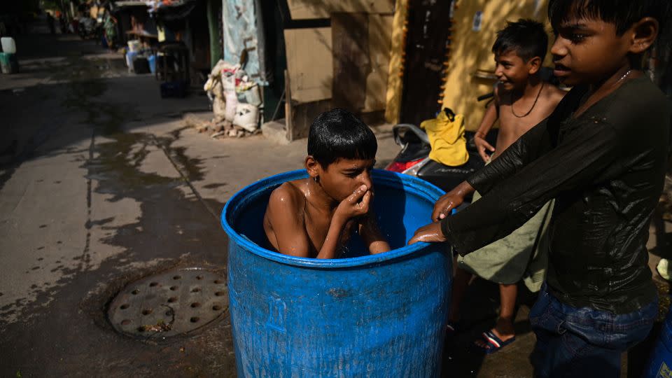 A boy takes a dip in a water container outside his slum dwelling in New Delhi, in May 2023. - Kabir Jhangiani/NurPhoto/Getty Images