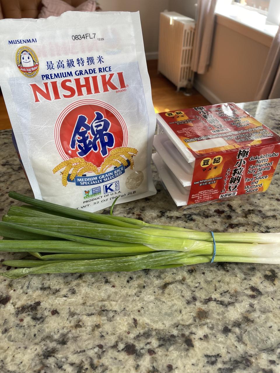 Bag of Nishiki rice, pack natto, and a bundle of green onions on a countertop