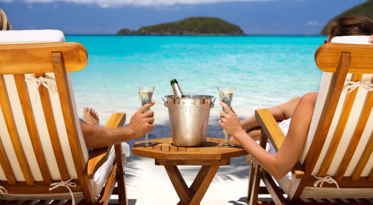 A pair of wealthy retirees enjoy Champagne on an exotic beach. 