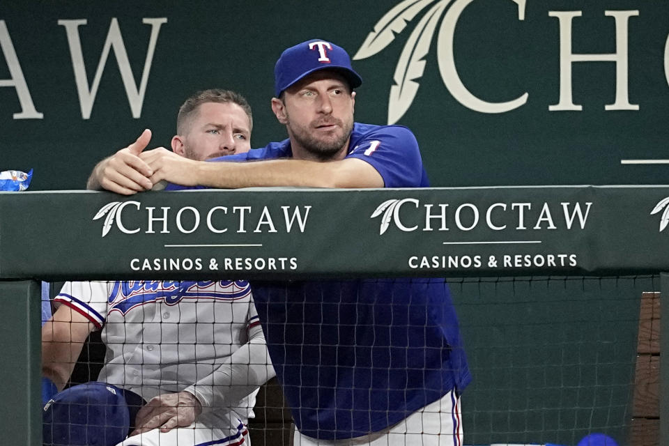 Texas Rangers newly acquired pitcher Max Scherzer, center, watches play from the dugout in the second inning of a baseball game against the Chicago White Sox, Tuesday, Aug. 1, 2023, in Arlington, Texas. (AP Photo/Tony Gutierrez)