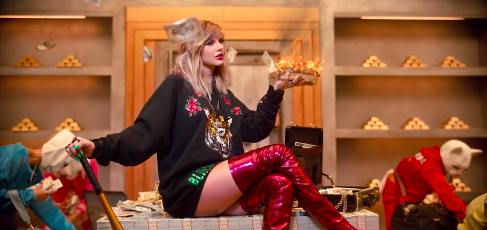 taylor sitting on a pile of money and holding a burning stack in her hand
