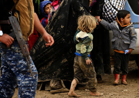 A displaced Iraqi child who fled his home with his family during a battle between Iraqi forces and Islamic State militants, walks with his mother at a checkpoint to be transfer to Hammam al-Alil camp, in Mosul, Iraq, March 20, 2017. REUTERS/Thaier Al-Sudani