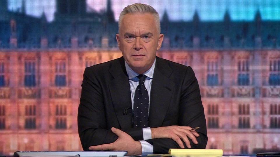 Huw Edwards sitting behind the desk in front of a Westminster backdrop while presenting the 2019 election results programme