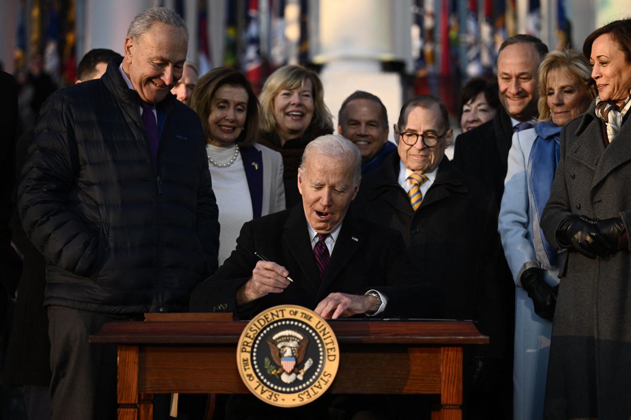 Surrounded by jubilant lawmakers, his spouse, Jill, and Vice President Kamala Harris and her husband, Doug Emhoff, President Biden gets ready to sign.