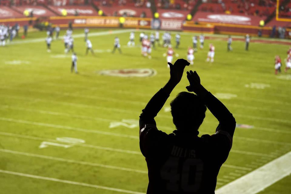 A silhouette of a fan clapping while football action takes place on the field.