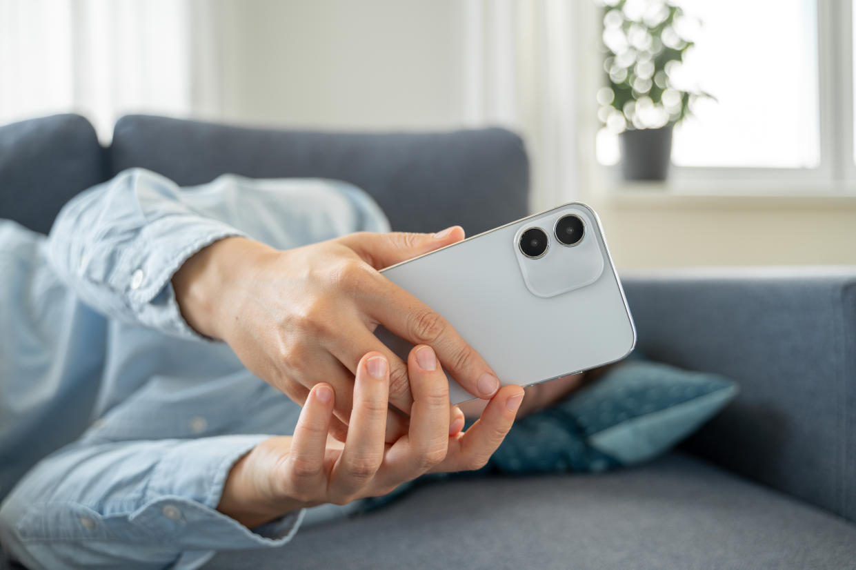 Tired Woman in blue shirt lying down on sofa after work, using smartphone. Fake dummy phone