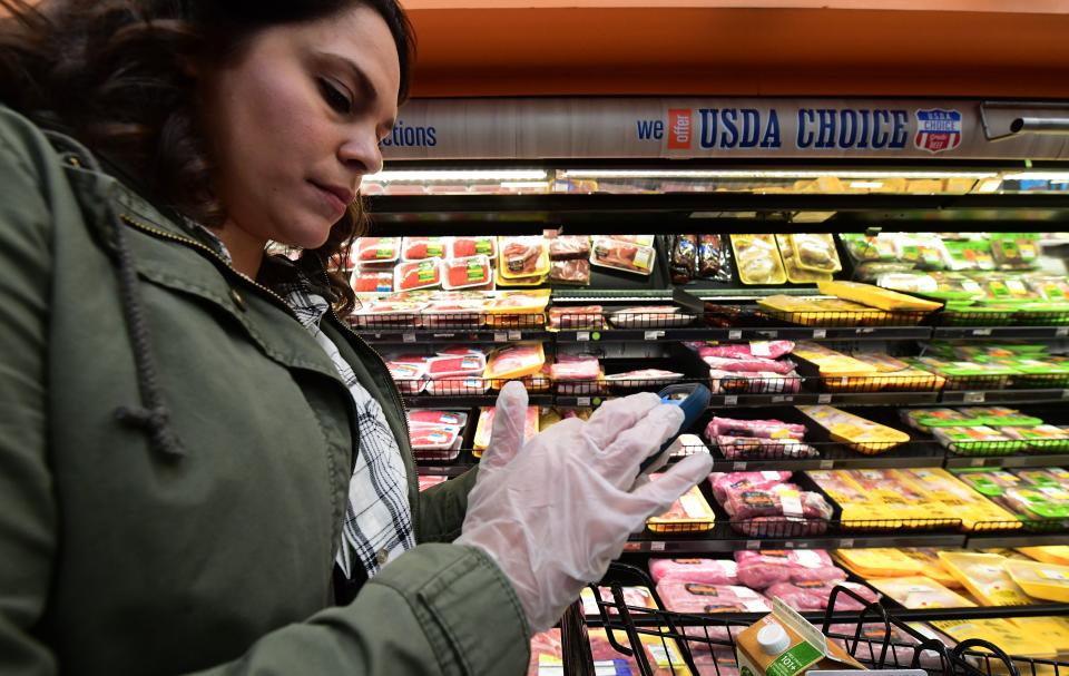 Instacart employee Monica Ortega wears gloves while using her cellphone to check orders while picking up groceries from a supermarket for delivery on March 19, 2020 in North Hollywood, California. (Photo by Frederic J. BROWN / AFP) (Photo by FREDERIC J. BROWN/AFP via Getty Images)