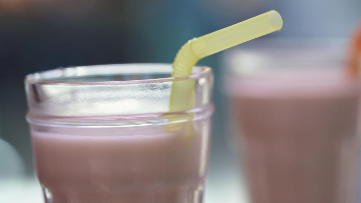 close up view of strawberry yogurt served in a glass tumbler with straw