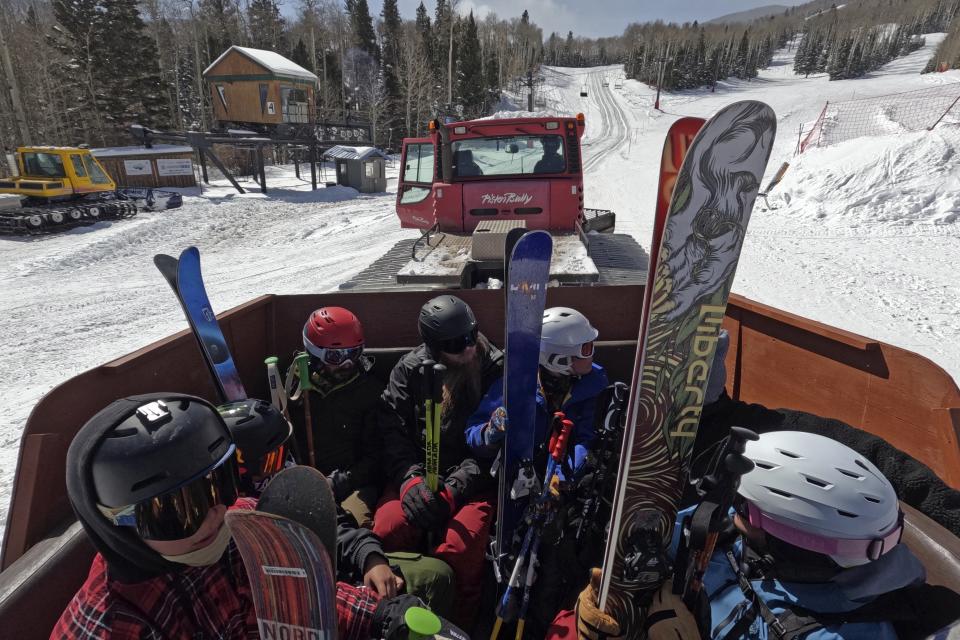 Riders wait to be towed up a ski hill at Parker-Fitzgerald Cuchara Mountain Park in a trailer retrofitted with old bus seats Sunday, March 19, 2023, near Cuchara, Colo. Some communities including Cuchara are now finding a niche, offering an alternative to endless lift lines and sky-high ticket prices. They're reopening, several as nonprofits, offering a mom-and-pop experience at a far lower cost than mountains run by corporate conglomerates. (AP Photo/Brittany Peterson)