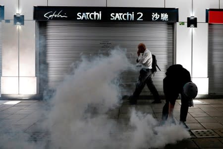 A man walks past an anti-extradition bill protester as he tries to pick up a tear gas canister at Tsim Sha Tsui after a demonstration in Hong Kong