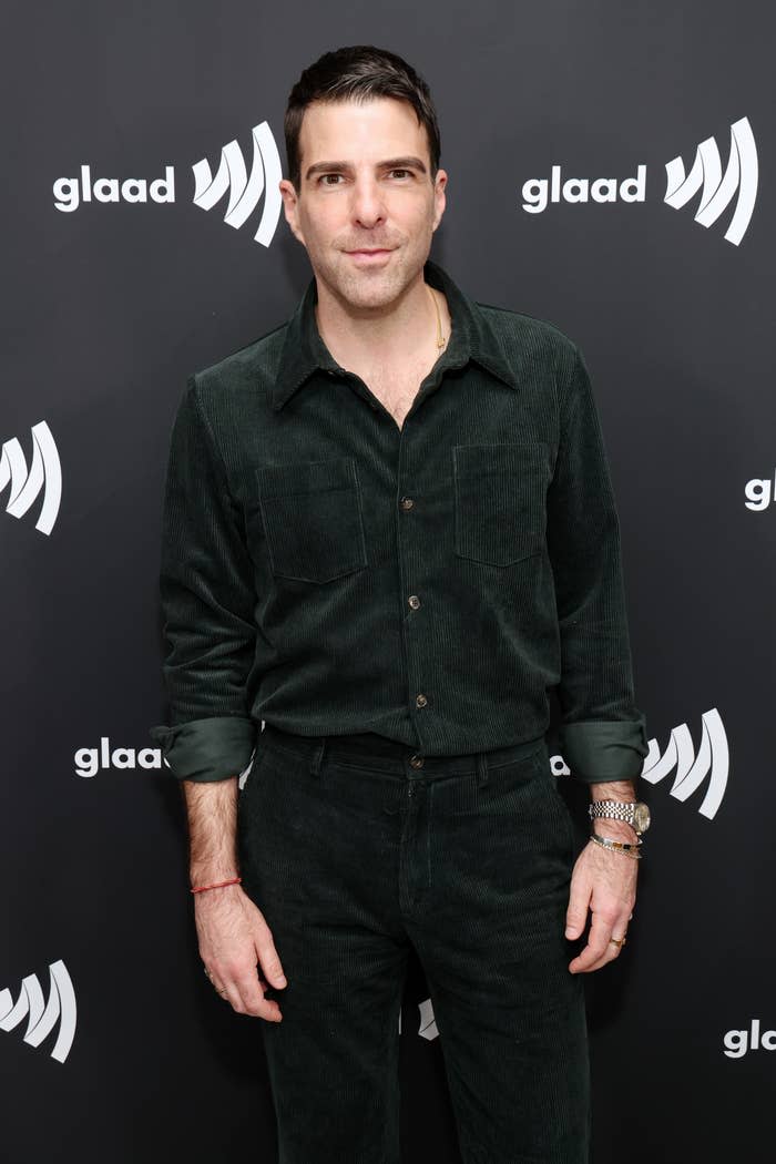 Zachary Quinto poses in a corduroy shirt and matching pants at a GLAAD event backdrop