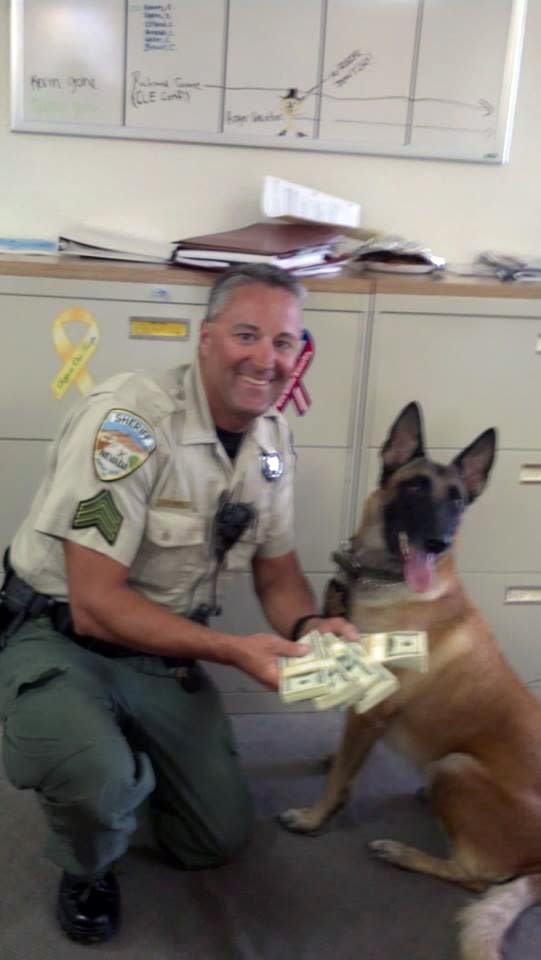 In this image released by the Humboldt County, Nev. Sheriff's Department in September 2013 and posted on their Facebook page, Sgt. Lee Dove poses with K-9 Zyla and $50,000 cash that was seized after a traffic stop for speeding. Dove is accused of stopping travelers on a lonely stretch of U.S. Interstate 80 and confiscating tens of thousands of dollars for the county without bringing charges, according to two federal lawsuits. Two men who were traveling alone through northern Nevada's high desert last year offer strikingly similar accounts of their stops by Dove near the town of Winnemucca, about 165 miles east of Reno. (AP Photo/Humboldt County Sheriff's Department)