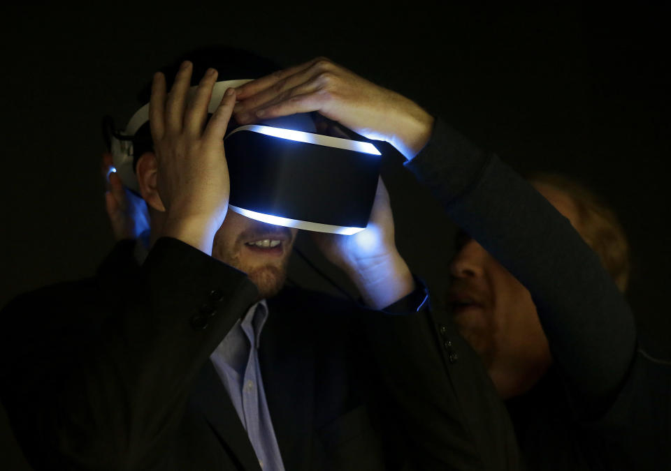 Kevin Joyce, left, gets help putting on the PlayStation 4 virtual reality headset Project Morpheus in a demo area at the Game Developers Conference 2014 in San Francisco, Wednesday, March 19, 2014. (AP Photo/Jeff Chiu)