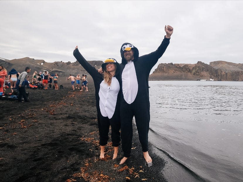 A man and woman in penguin suits by a grey beach.