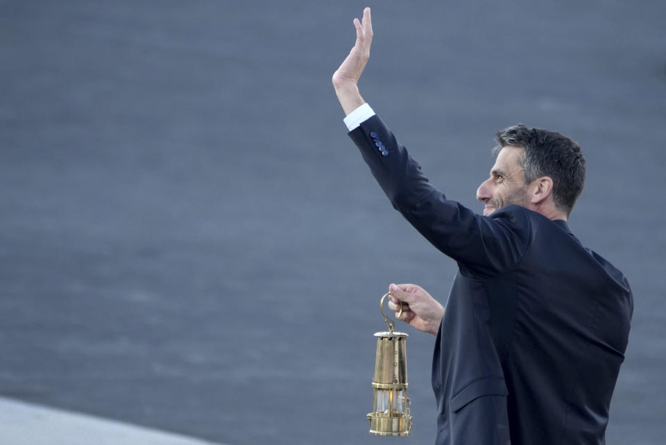 Tony Estanguet, President of Paris 2024, waves while holding the Olympic flame during the flame handover ceremony at Panathenaic stadium, where the first modern games were held in 1896, in Athens, Friday, April 26, 2024. On Saturday the flame will board the Belem, a French three-masted sailing ship, built in 1896, to be transported to France. (AP Photo/Petros Giannakouris)