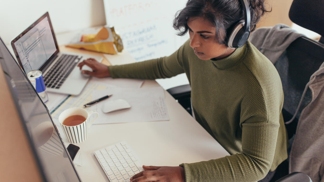 Female programmer coding on a desktop computer and laptop at her desk in office.