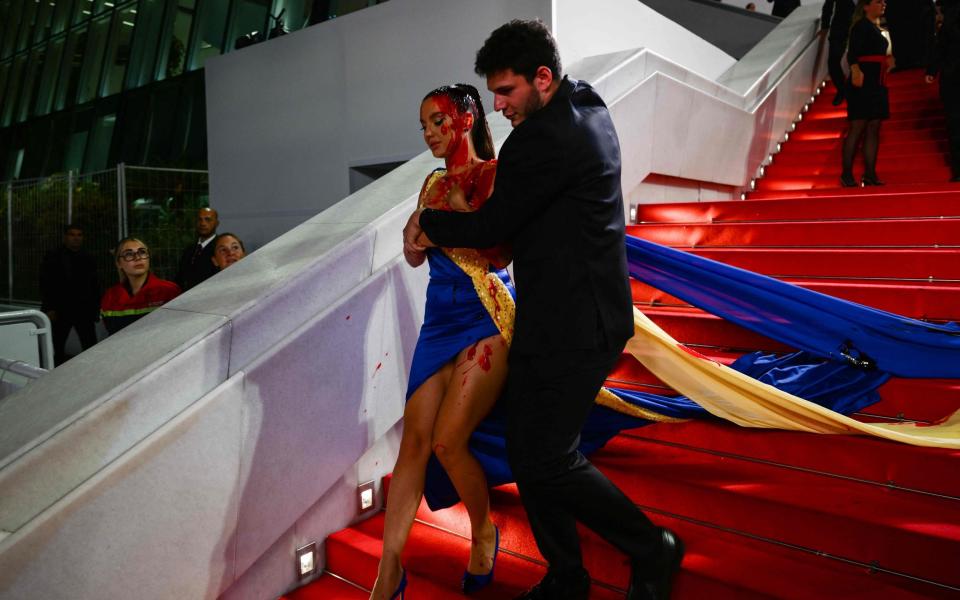 A protester, wearing a dress in the colours of the Ukrainian flag, is detained by security after she covered herself in fake blood on the stairs on the Festival Palace ahead of the screening of the film "Acide" in Cannes - CHRISTOPHE SIMON/AFP