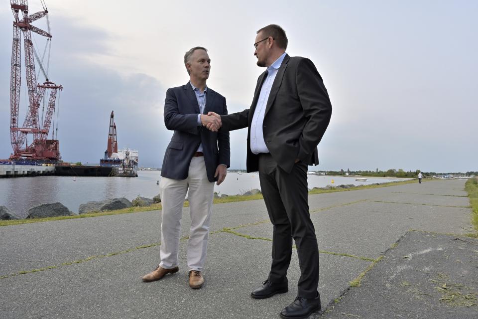 New Bedford Mayor Jon Mitchell, left, and Vineyard Wind CEO Klaus Skoust Moeller shake hands in front of the ship UHL Felicity, which docked in New Bedford Harbor, Wednesday, May 24, 2023, in Bedford, Mass. The vessel carried massive parts for offshore wind turbines. (AP Photo/Josh Reynolds)